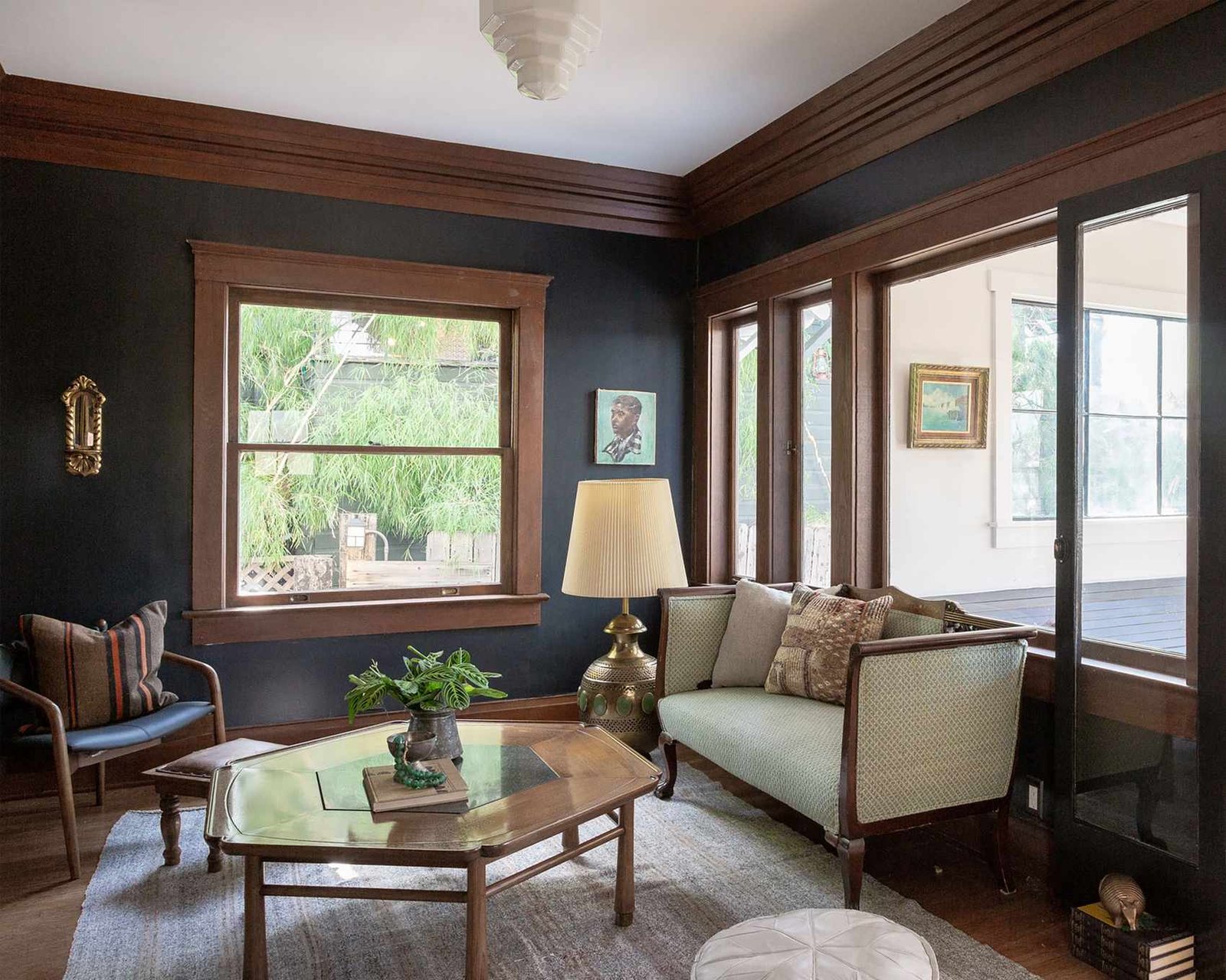 Traditional living room with dark wood detailing on trims, dark wood flooring, gray rug, dark wood coffee table, small sofa and chair with dark wood frame, internal windows looking onto hallway